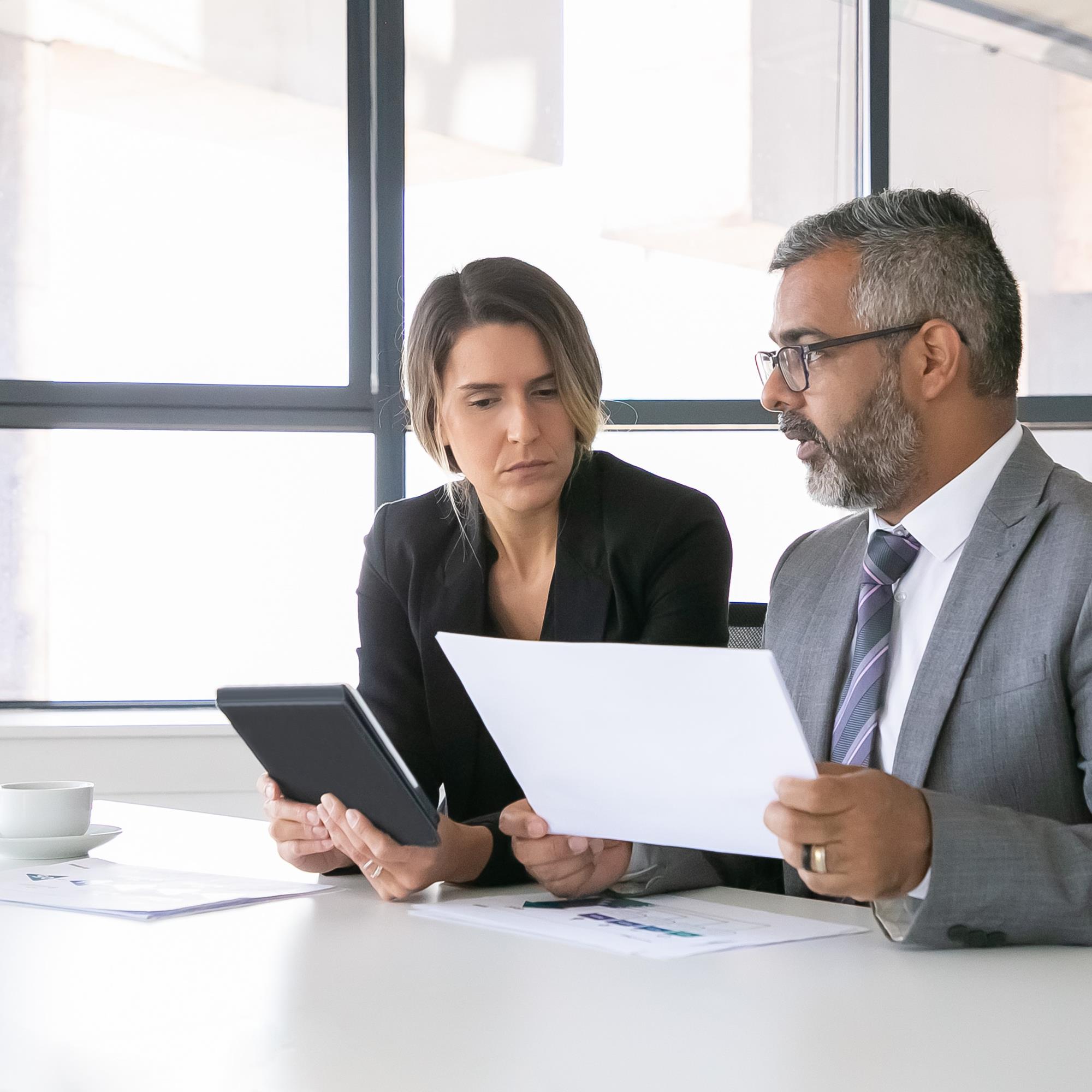 Company Leaders Analyzing Reports Two Business Colleagues Sitting Together Looking Document Holding Tablet Talking Medium Shot Communication Concept